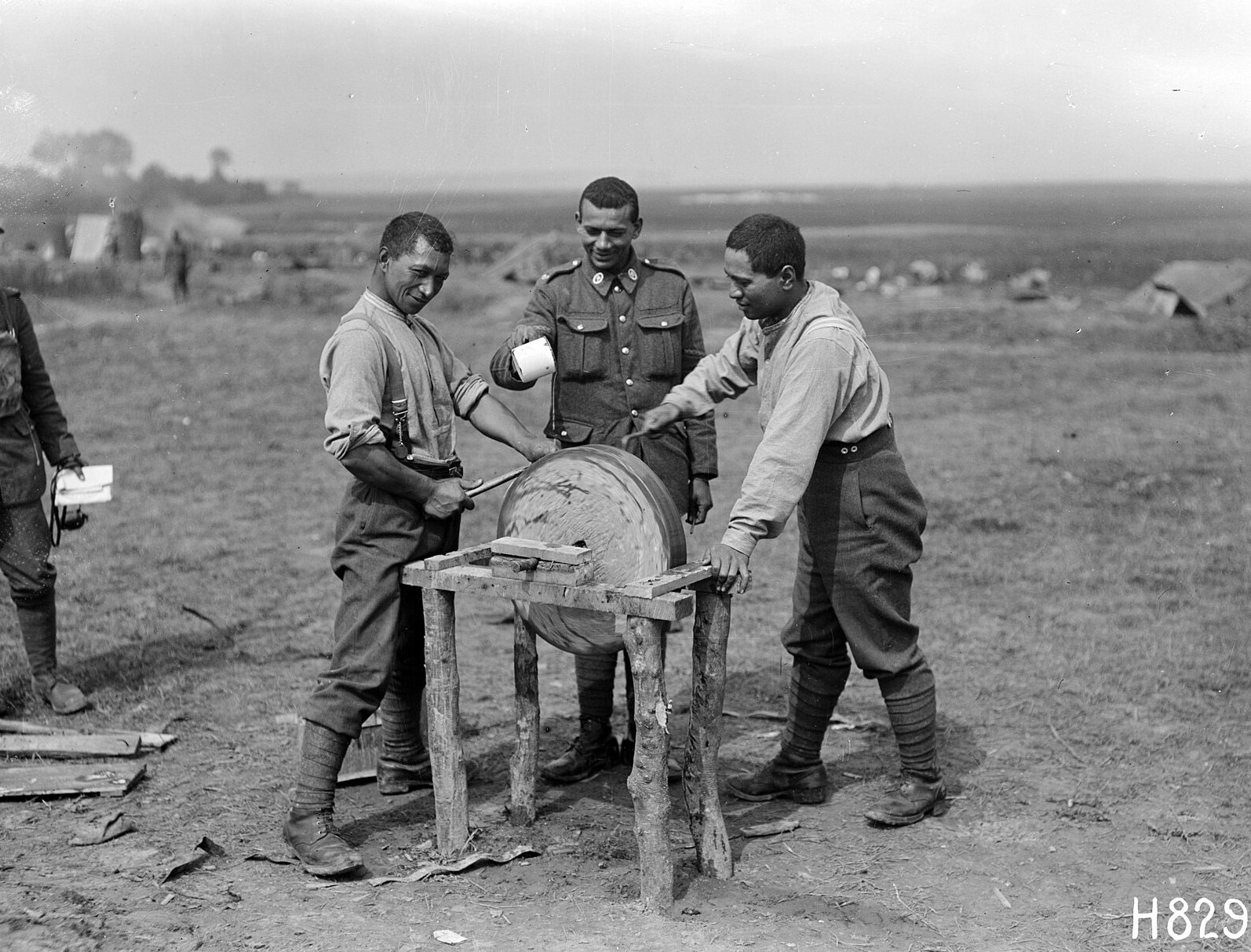 Three Māori Pioneer Battalion soldiers sharpening a hatchet on a grindstone at their camp at Bayencourt, France, 1918